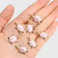 Gold-tone 24mm turtle charms with pink flower shells held in a palm