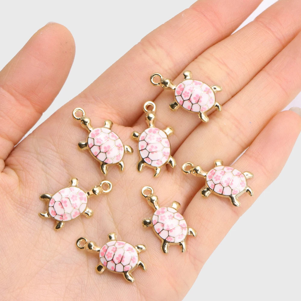 Gold-tone 24mm turtle charms with pink flower shells held in a palm