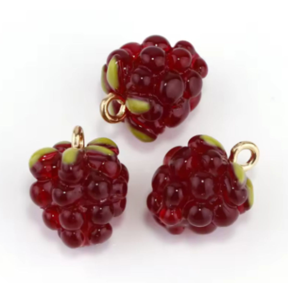 Close-up of two red resin berry charms with green tops and gold-tone loops