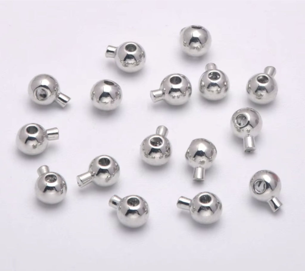 Pile of rhodium stopper crimp beads with loops on a pale background