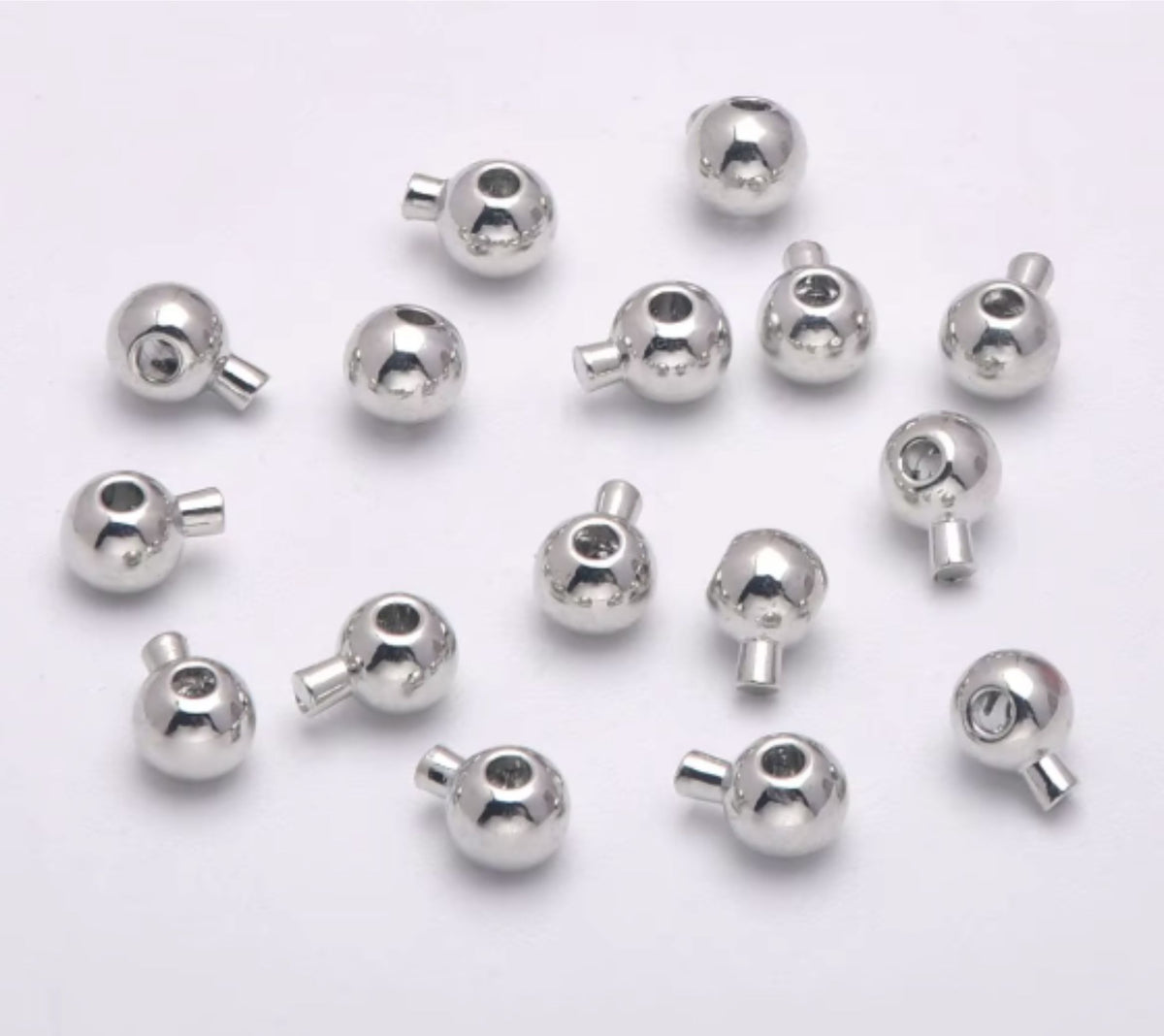 Pile of rhodium stopper crimp beads with loops on a pale background