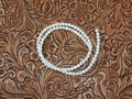 Strand of 4mm round white mother of pearl beads on a tooled leather background