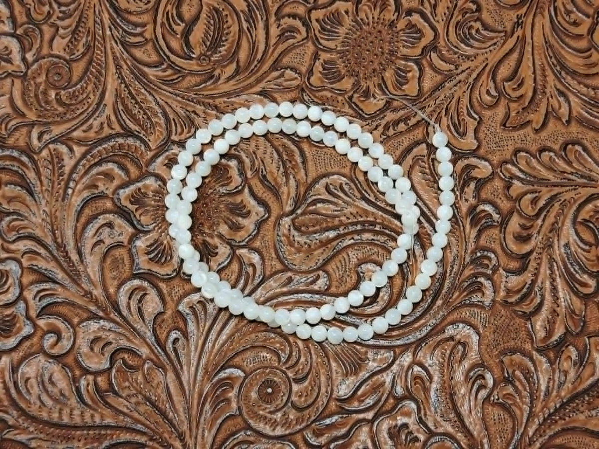 Strand of 4mm round white mother of pearl beads on a tooled leather background