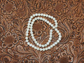 Strand of 6mm round white mother of pearl beads on a tooled leather background