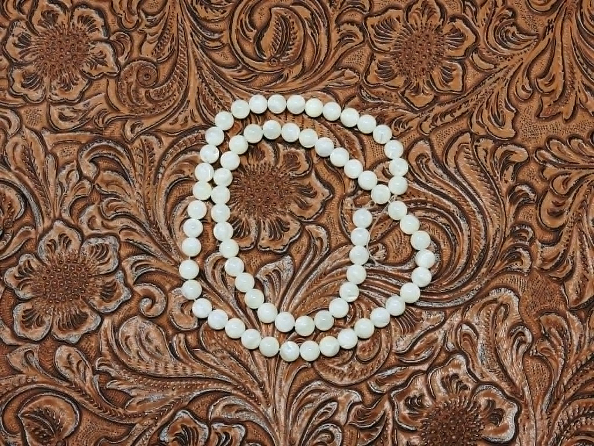 Strand of 6mm round white mother of pearl beads on a tooled leather background
