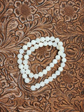 Strand of 8mm round white mother of pearl beads on a tooled leather background