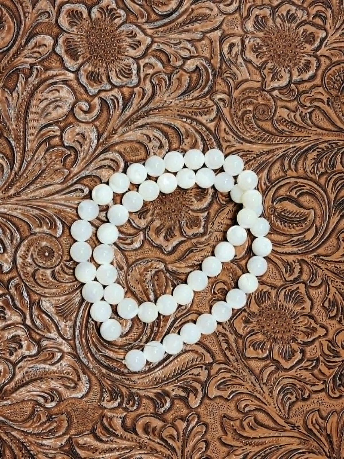 Strand of 8mm round white mother of pearl beads on a tooled leather background
