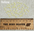 Fifty 5mm yellow pearl-look resin half round cabochons (cabs) scattered beside a ruler