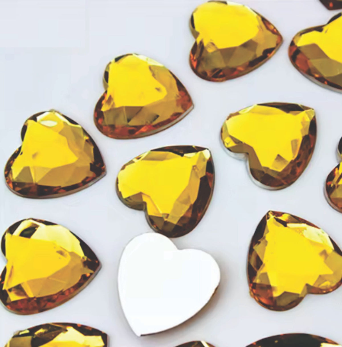 Pile of 20mm faceted yellow resin heart gem cabochons (cabs), one flipped to show the flat back