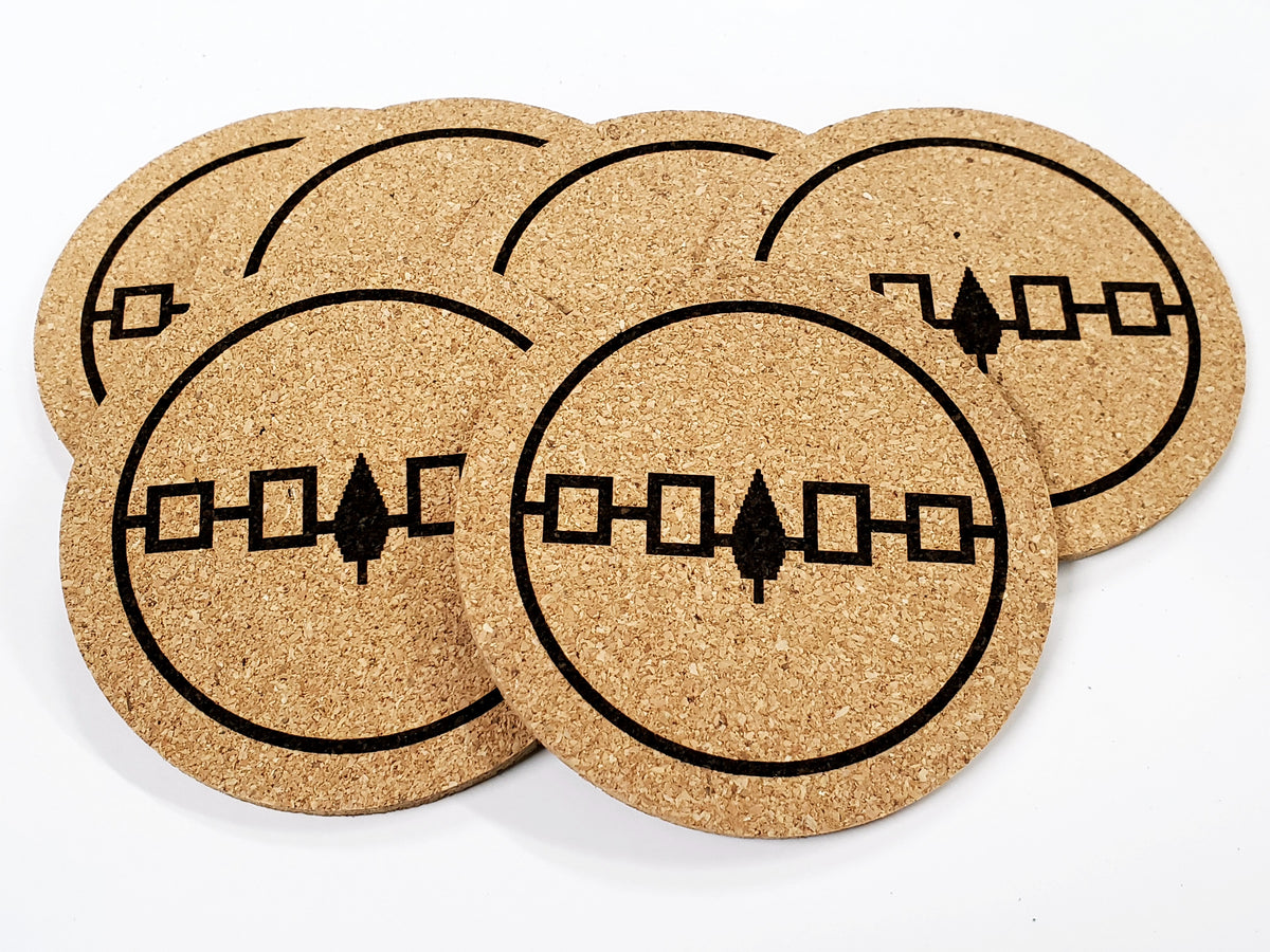 Stack of round cork coasters printed in black with a Five Nations belt band of squares and a tree