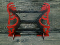 Kokapeli-shaped earring display rack with rows of holes, in red with a black centre