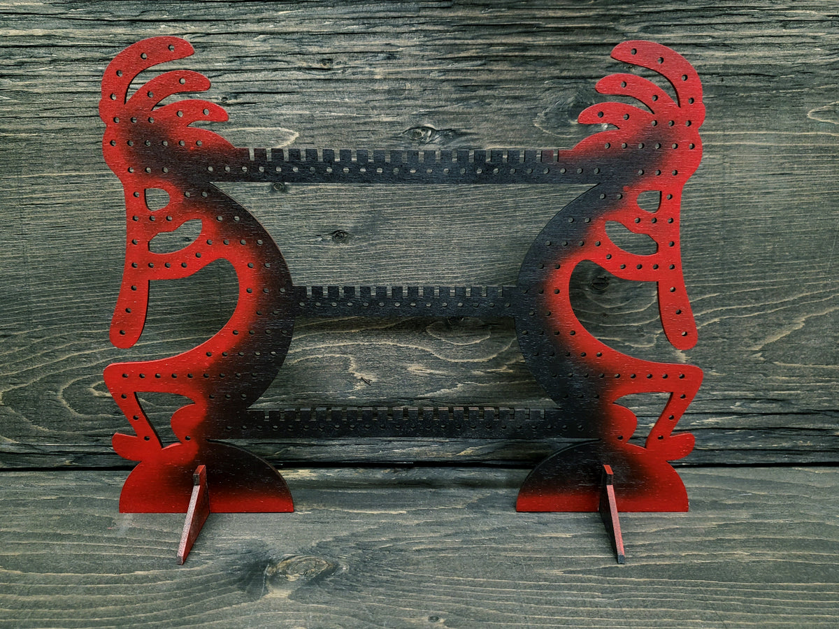 Kokapeli-shaped earring display rack with rows of holes, in red with a black centre