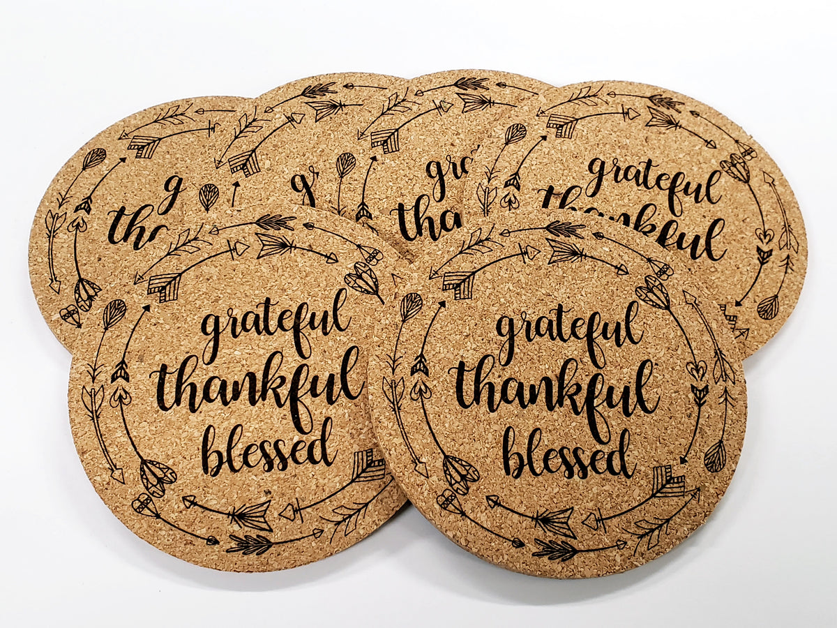 Stack of round cork coasters printed with the words 'grateful, thankful, blessed'