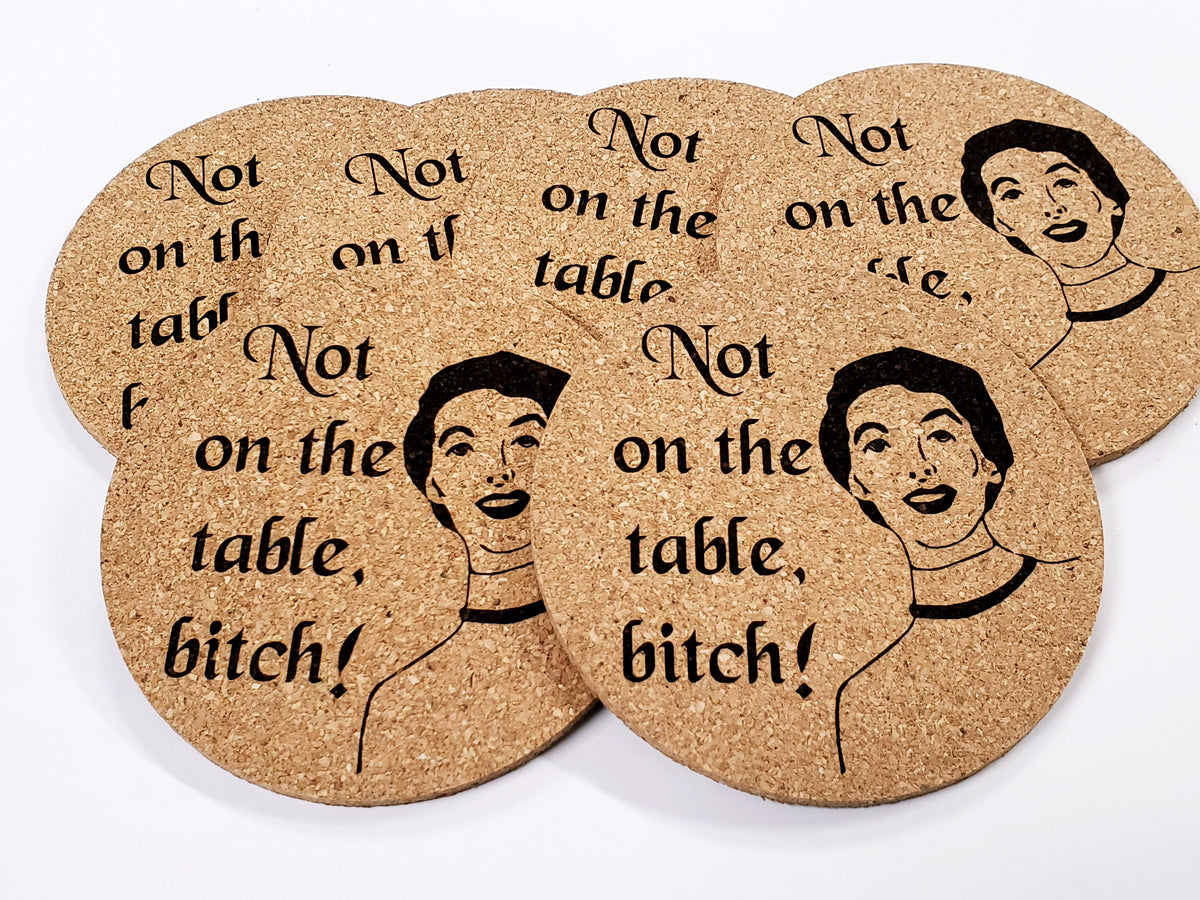 Stack of round cork coasters printed with the words 'Not on the table, bitch!' beside a retro woman