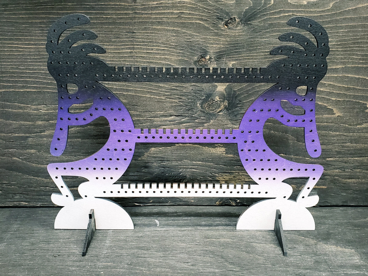 Kokapeli-shaped earring display rack with rows of holes, in black to purple to white