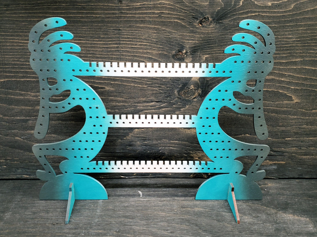 Kokapeli-shaped earring display rack with rows of holes, in white, turquoise and grey