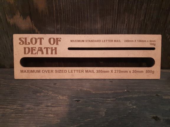 Wooden Canada Post size slot labelled Slot of Death, with standard and oversized letter gaps