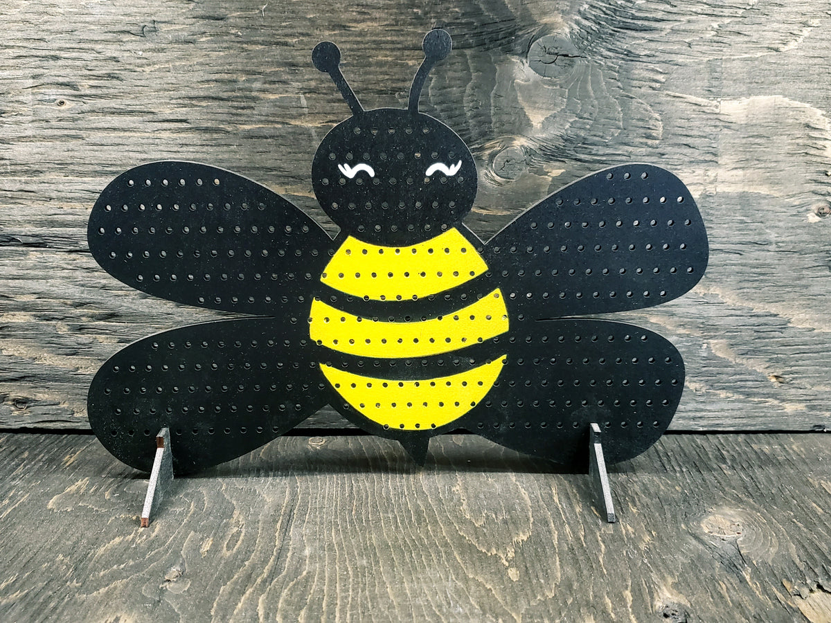 Bee-shaped earring display rack with black wings, a yellow and black striped body and a smiling face